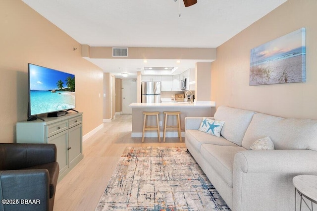 living room featuring sink, light hardwood / wood-style flooring, and ceiling fan