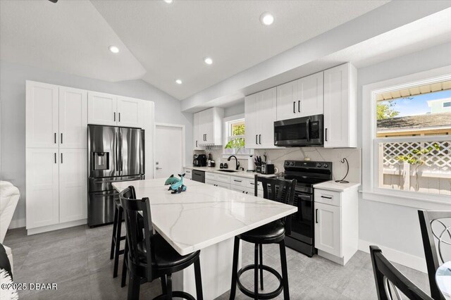 5967 Riverside Dr, Port Orange, FL 32127 - kitchen with black appliances, backsplash, a breakfast bar area, a center island, and vaulted ceiling