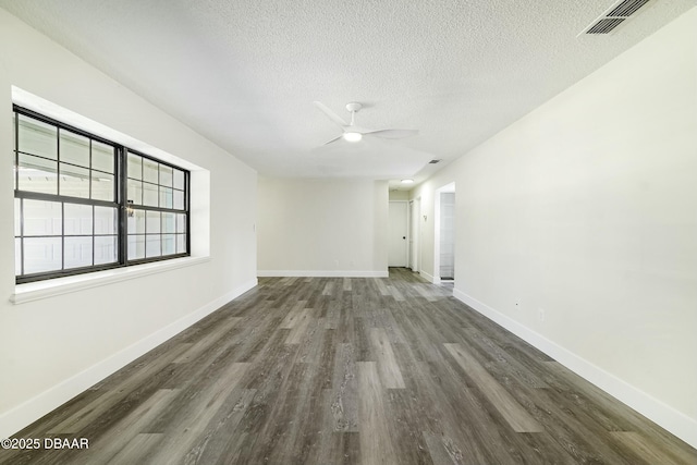 unfurnished room with a textured ceiling, wood finished floors, visible vents, and baseboards