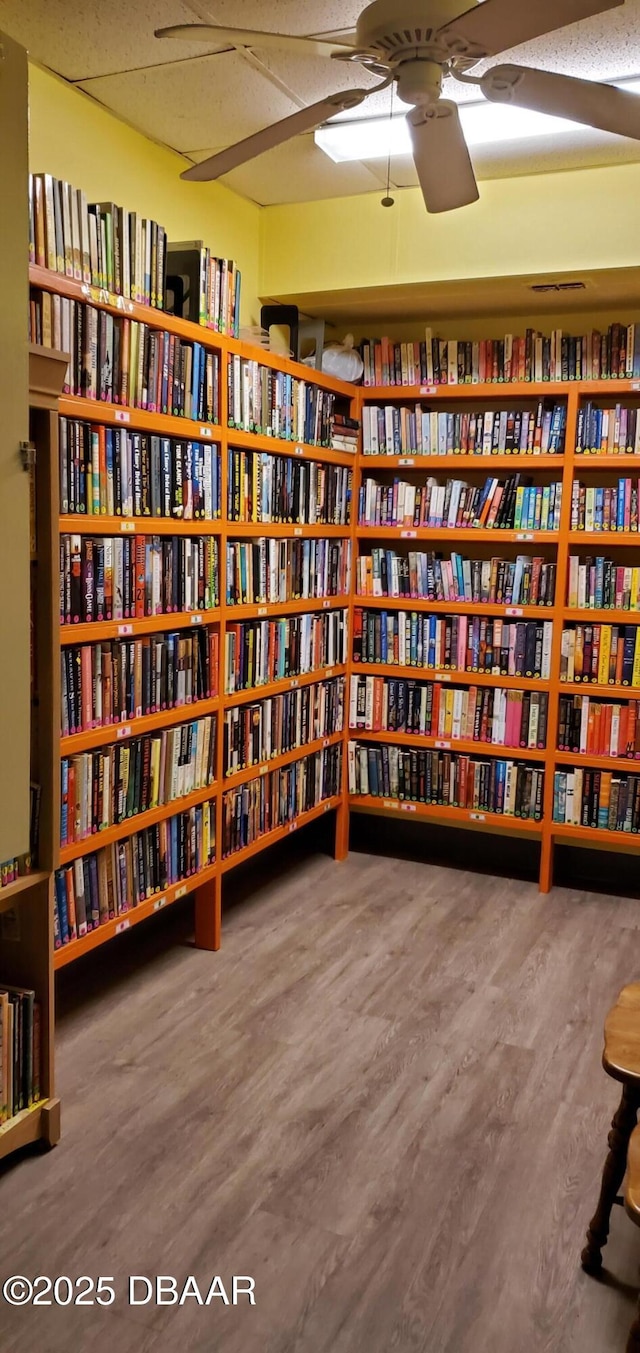 unfurnished room featuring a ceiling fan, wall of books, and wood finished floors