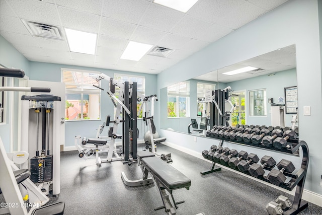 exercise room with a paneled ceiling, visible vents, and baseboards