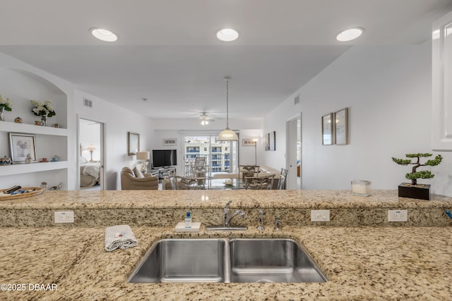 kitchen featuring light stone counters, visible vents, a sink, and a ceiling fan