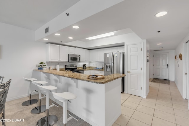 kitchen featuring stone countertops, a peninsula, stainless steel appliances, a kitchen bar, and white cabinetry