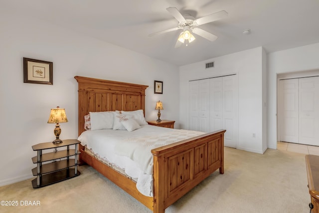 bedroom with light carpet, baseboards, visible vents, a ceiling fan, and two closets