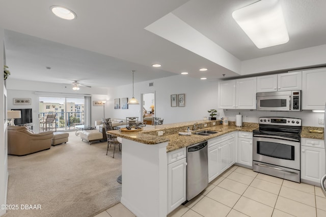 kitchen with stainless steel appliances, a peninsula, a sink, white cabinets, and open floor plan