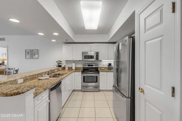 kitchen with light tile patterned flooring, a peninsula, a sink, white cabinetry, and appliances with stainless steel finishes