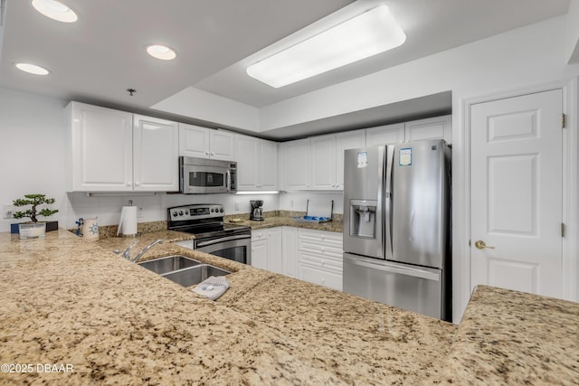 kitchen with stainless steel appliances, a sink, light stone countertops, and white cabinets