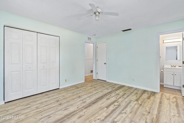 unfurnished bedroom featuring sink, ensuite bath, ceiling fan, a closet, and light wood-type flooring