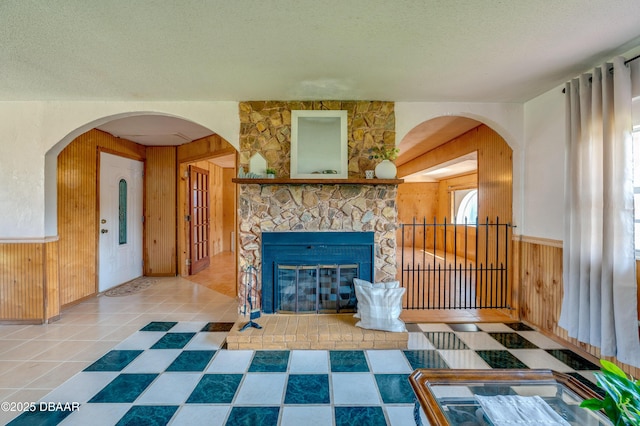 living room featuring a stone fireplace, tile patterned floors, a textured ceiling, and wood walls