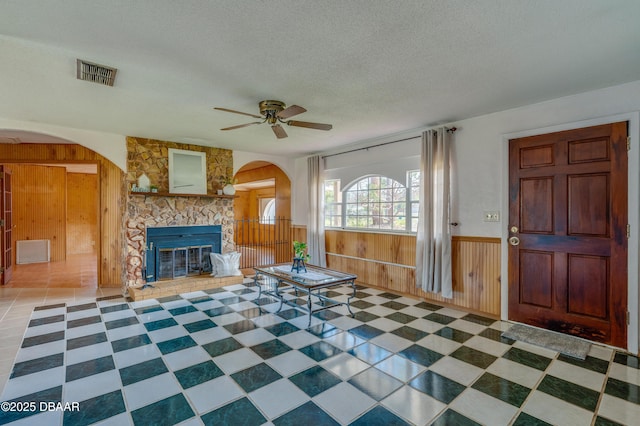 unfurnished living room featuring ceiling fan, a fireplace, a textured ceiling, and wood walls