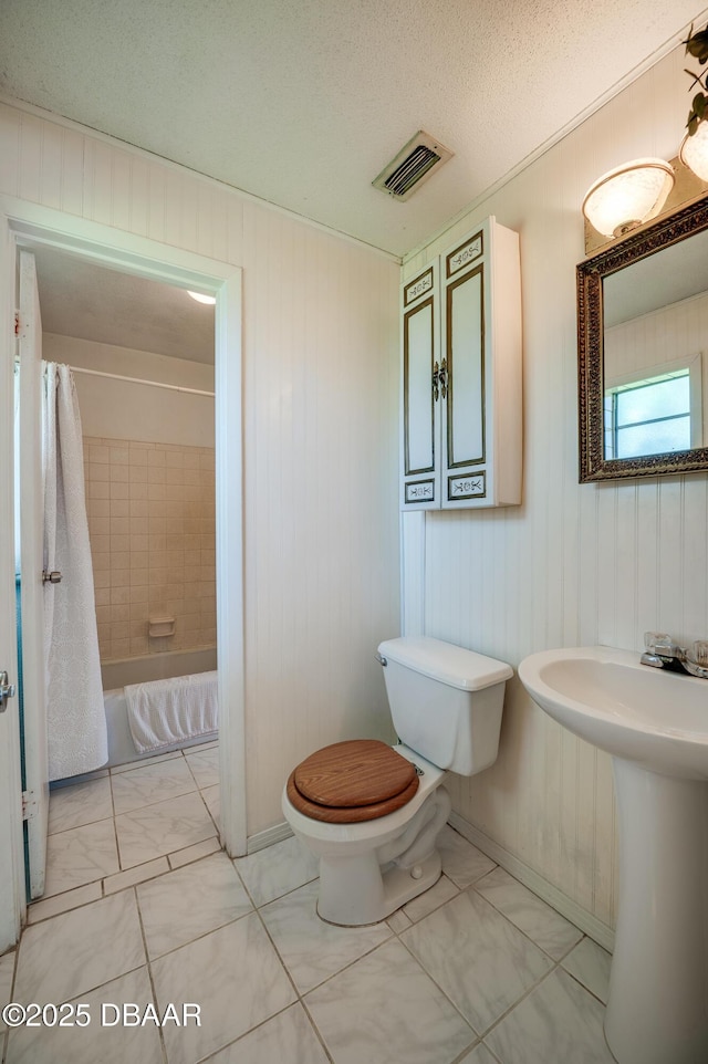 bathroom featuring shower / bath combination with curtain, toilet, and a textured ceiling