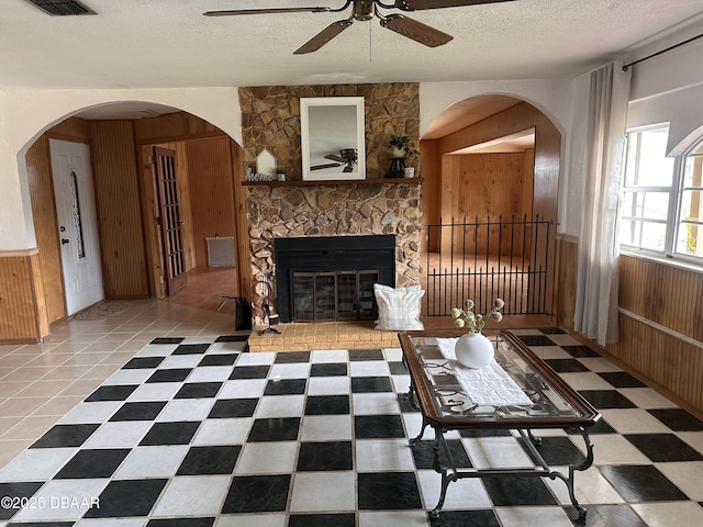 living room featuring ceiling fan, a fireplace, a textured ceiling, and wood walls