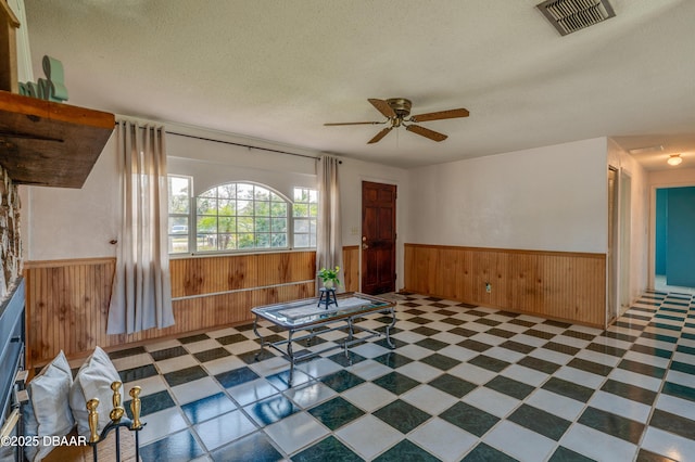 interior space featuring ceiling fan, a textured ceiling, and wood walls