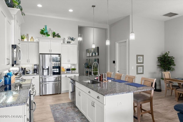 kitchen featuring pendant lighting, appliances with stainless steel finishes, white cabinetry, sink, and a center island with sink