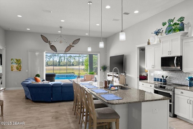 kitchen with hanging light fixtures, appliances with stainless steel finishes, sink, white cabinets, and a kitchen island with sink