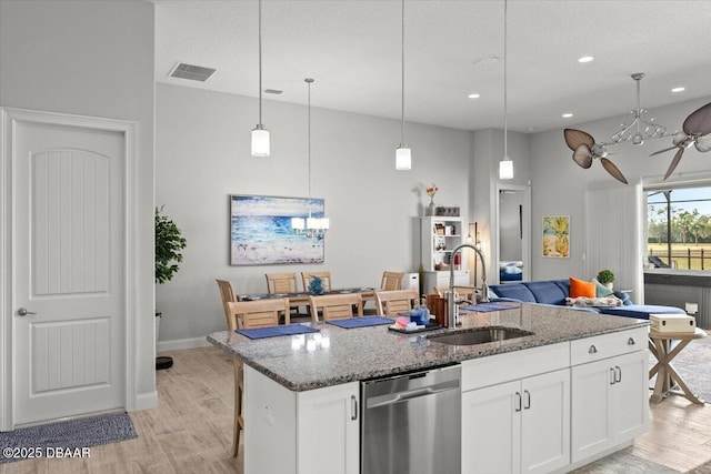 kitchen featuring white cabinetry, a kitchen island with sink, stainless steel dishwasher, sink, and light stone counters