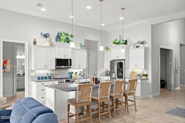 kitchen with white cabinets, a kitchen island with sink, hanging light fixtures, and appliances with stainless steel finishes