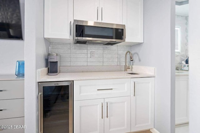 kitchen featuring tasteful backsplash, stainless steel microwave, wine cooler, light countertops, and white cabinetry