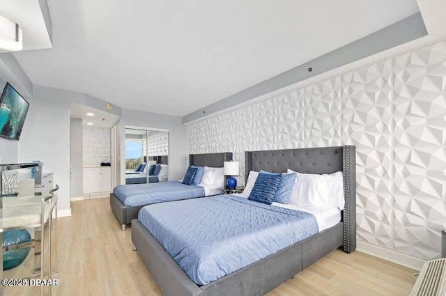 bedroom featuring baseboards, wood finished floors, an accent wall, and wallpapered walls