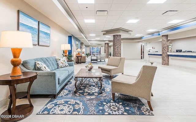 living area featuring a drop ceiling, visible vents, and ornate columns