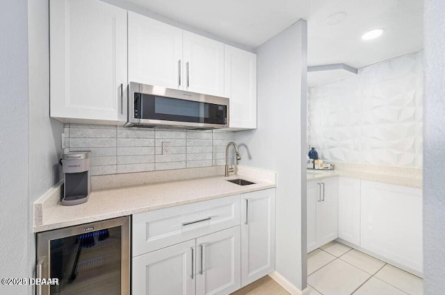 kitchen with beverage cooler, a sink, decorative backsplash, white cabinets, and stainless steel microwave