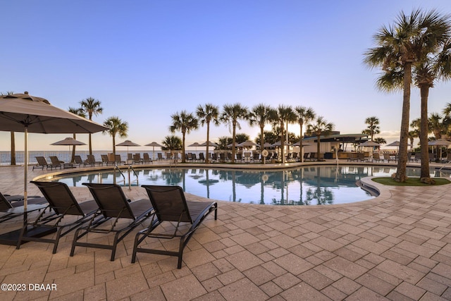 pool at dusk with a water view and a patio area