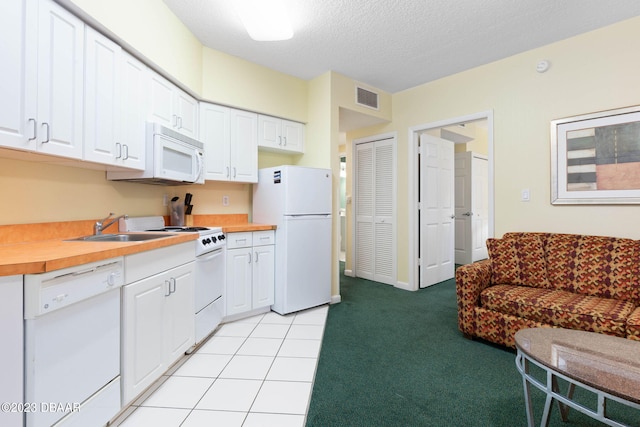 kitchen featuring wooden counters, a textured ceiling, light carpet, white cabinets, and white appliances