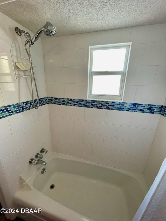 bathroom with a textured ceiling and tiled shower / bath combo