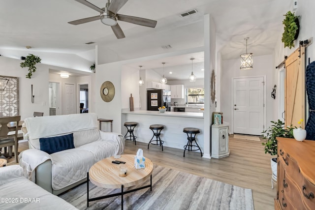 living room with visible vents, ceiling fan, light wood-type flooring, a barn door, and vaulted ceiling