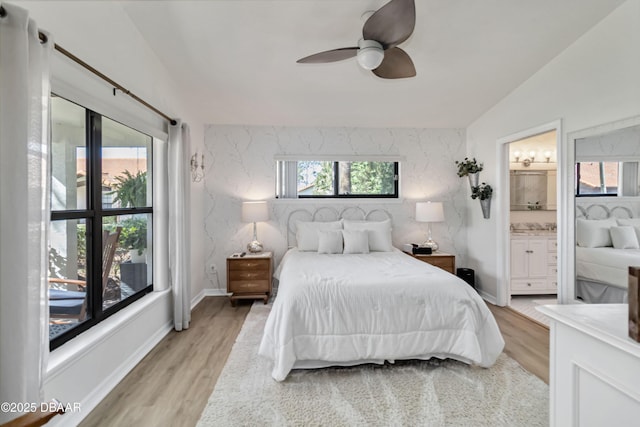 bedroom with light wood finished floors, ceiling fan, baseboards, vaulted ceiling, and ensuite bath