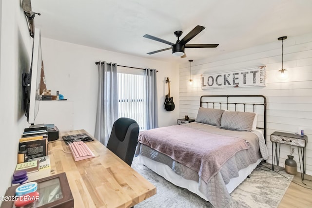 bedroom featuring wooden walls, a ceiling fan, and wood finished floors