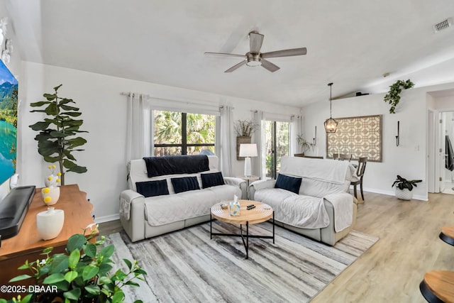 living area featuring wood finished floors, a ceiling fan, visible vents, baseboards, and lofted ceiling