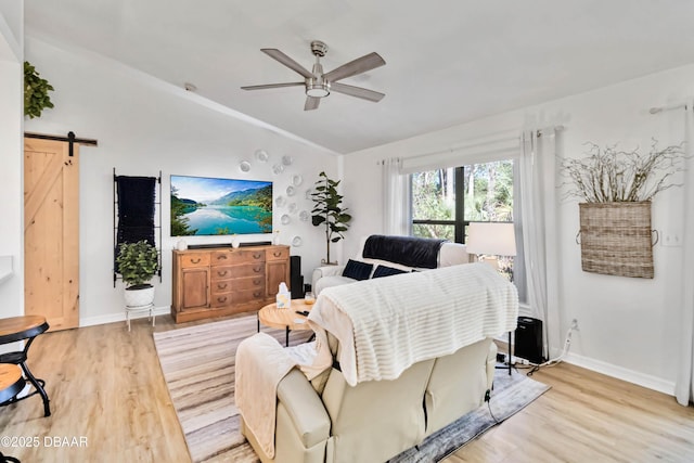 living room with a barn door, baseboards, a ceiling fan, and light wood finished floors