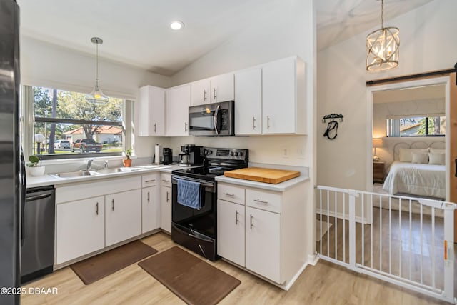 kitchen featuring lofted ceiling, light wood-style flooring, appliances with stainless steel finishes, white cabinets, and a sink