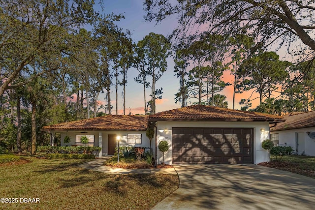 view of front facade with a tiled roof, concrete driveway, stucco siding, a yard, and a garage