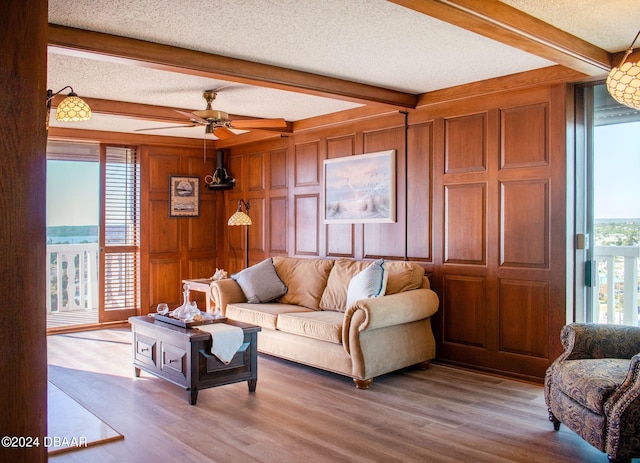 living room featuring beam ceiling, a textured ceiling, light hardwood / wood-style flooring, and wood walls