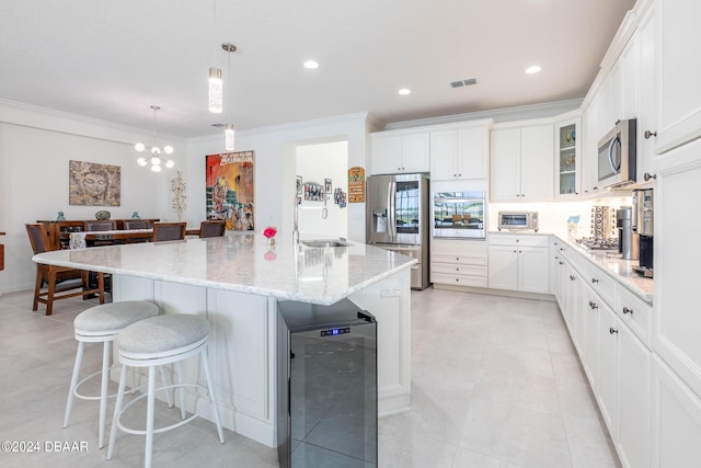 kitchen with stainless steel appliances, wine cooler, decorative light fixtures, an island with sink, and white cabinets