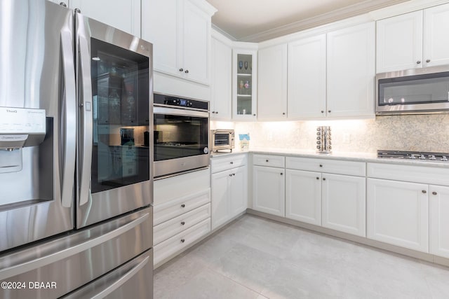 kitchen with light tile patterned flooring, appliances with stainless steel finishes, ornamental molding, white cabinets, and decorative backsplash