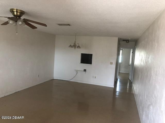 empty room featuring a textured ceiling and ceiling fan with notable chandelier