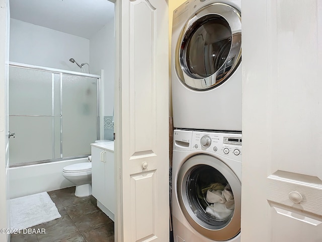 laundry area with dark tile patterned floors and stacked washer and dryer