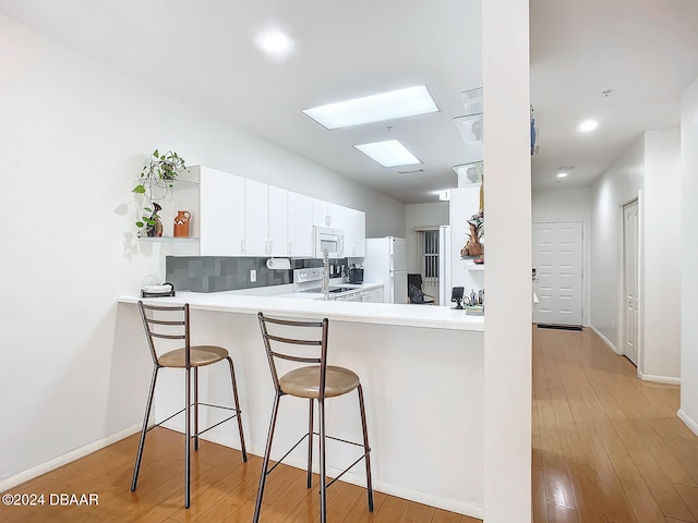 kitchen featuring light hardwood / wood-style floors, white cabinets, kitchen peninsula, a breakfast bar, and white appliances