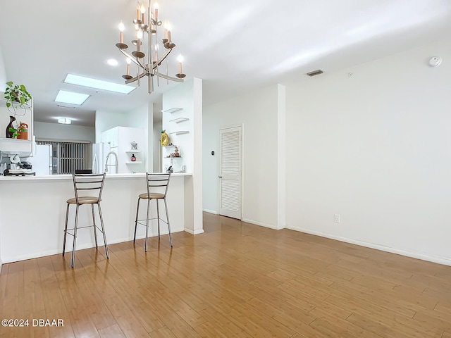 kitchen with white refrigerator, white cabinets, kitchen peninsula, a chandelier, and light hardwood / wood-style flooring