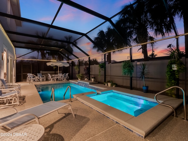 pool at dusk featuring a patio, glass enclosure, and a hot tub