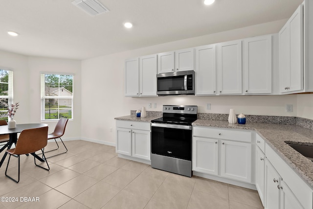 kitchen featuring stainless steel appliances, light stone countertops, white cabinetry, and light tile patterned floors