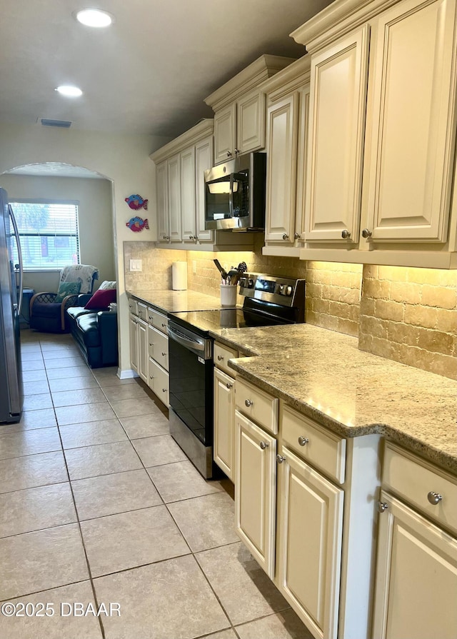 kitchen with light tile patterned flooring, light stone counters, backsplash, stainless steel appliances, and cream cabinetry