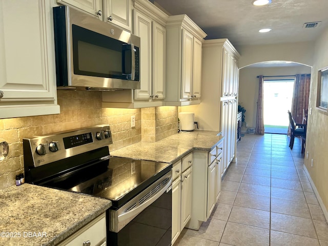 kitchen featuring stainless steel appliances, tasteful backsplash, light tile patterned flooring, and light stone counters