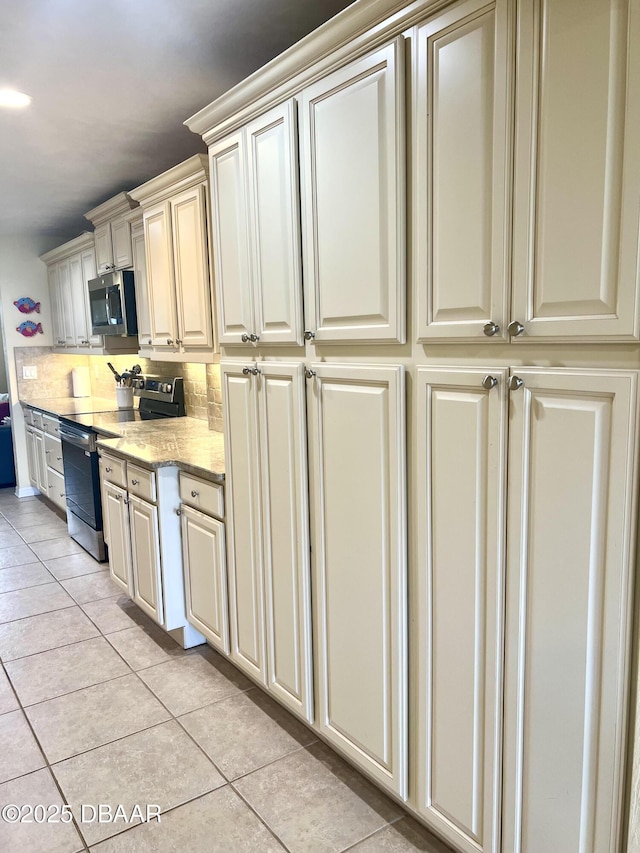 kitchen with light tile patterned flooring, appliances with stainless steel finishes, tasteful backsplash, light stone countertops, and cream cabinetry