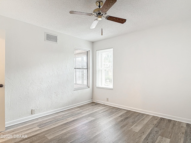 empty room featuring light wood-type flooring, visible vents, a textured ceiling, and baseboards