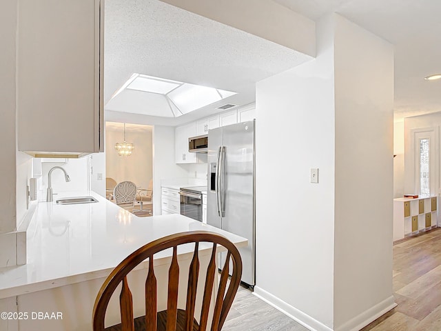 kitchen with a sink, white cabinetry, light countertops, appliances with stainless steel finishes, and light wood-type flooring