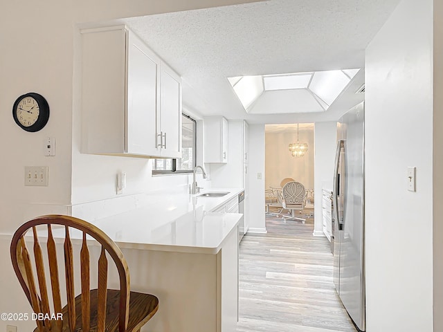 kitchen with a peninsula, a sink, white cabinets, light countertops, and light wood finished floors